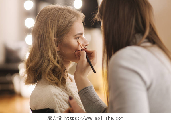 化妆室内化妆师给顾客画眼影特写化妆艺术家在她的美容室里工作.由专业化妆大师申请的女性肖像.美丽的化妆师开始为金发模特化妆